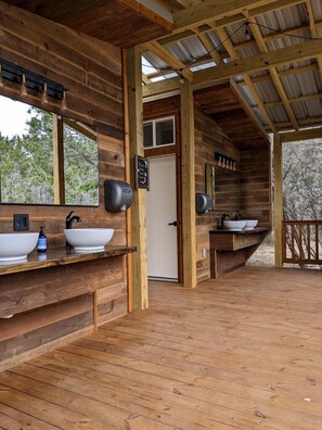 A wooden cabin with a bathroom featuring two sinks, a mirror, and a door. - Romantic Getaways in Fully-Equipped Tree House Rental in Spicewood, Texas (Spicewood)