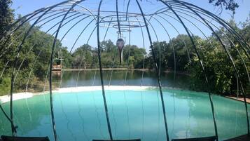 A pool with a metal structure overhead, surrounded by trees and a clear sky.