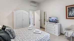 Ein Schlafzimmer mit einem Bett, einem Schminktisch, einem Fernseher und einem gerahmten Bild an der Wand.