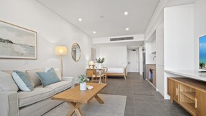 A modern living room with a sofa, coffee table, and dining area. There is a TV on the right and a kitchen in the background. - Chic Ground-floor Studio Near Local Cafes (Perth)