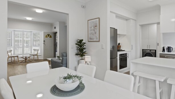 A modern kitchen with white cabinetry, a dining area with a white table and chairs, and a living area with a sofa and a coffee table. - Beachside 3-bed Retreat With BBQ & Garage (Adelaide)