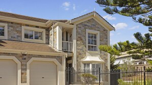 A two-story house with a stone facade, a balcony, and a black metal fence. - Beachside 3-bed Retreat With BBQ & Garage (Adelaide)