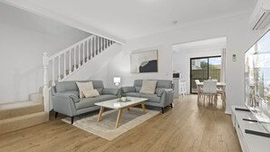 A modern living room with a grey sofa, a white coffee table, and a staircase. - Beachside 3-bed Retreat With BBQ & Garage (Adelaide)