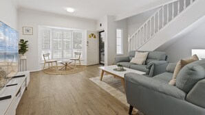 A modern living room with a grey sofa, a coffee table, and a dining area with chairs and a table. - Beachside 3-bed Retreat With BBQ & Garage (Adelaide)