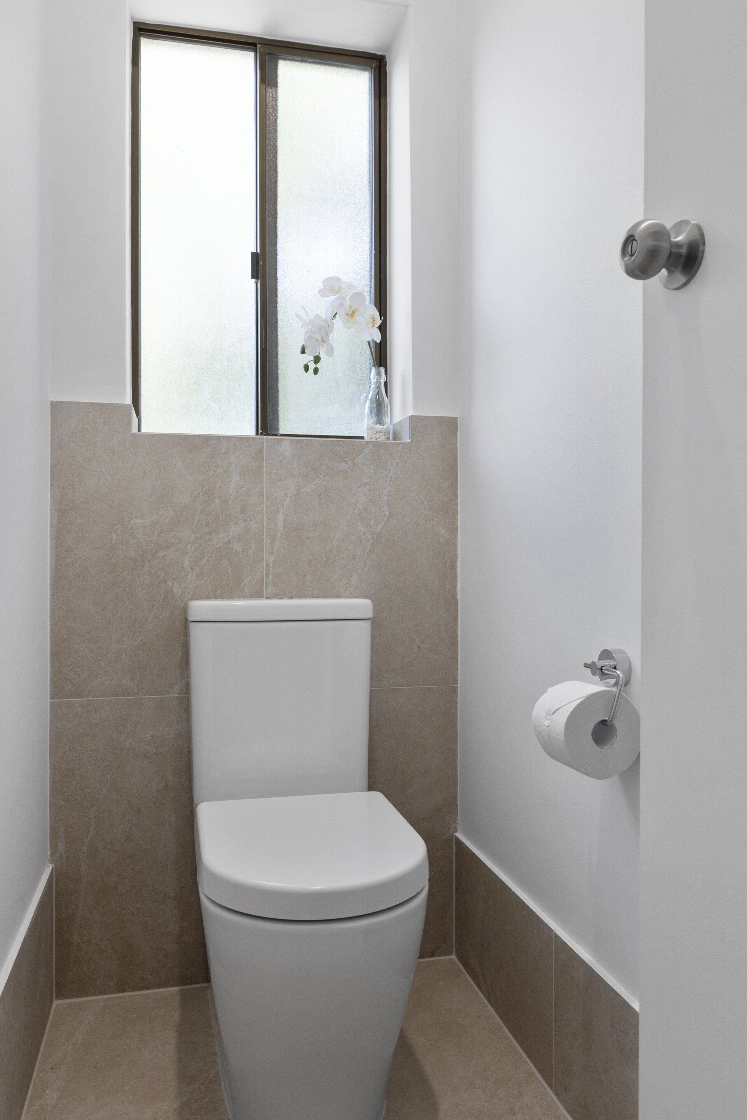 Une salle de bain moderne équipée de toilettes, d’une fenêtre et d’un porte-rouleau de papier toilette.