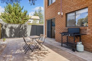 Een terras buiten met een barbecue en opklapbare stoelen.