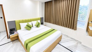 Quarto de hotel moderno com uma cama grande, mesa de cabeceira, cortinas e janela.