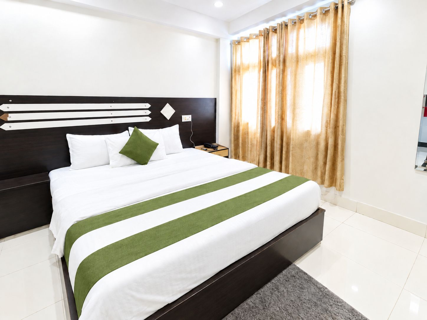 A hotel room with a large bed, a headboard with horizontal lines, a nightstand, and a window with curtains.