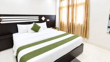 A hotel room with a large bed, a headboard with horizontal lines, a nightstand, and a window with curtains.