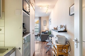 A compact kitchen with a built-in oven, a dining area with a table and chairs, and a living space with a sofa and a lamp.