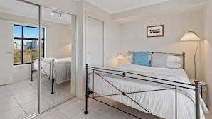 Ein Schlafzimmer mit einem Bett, einem Nachttisch, einer Lampe, einem Bild an der Wand und einer Schiebetür, die auf einen Balkon führt.