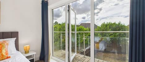 A bedroom with a large sliding glass door leading to a balcony with a wooden deck.