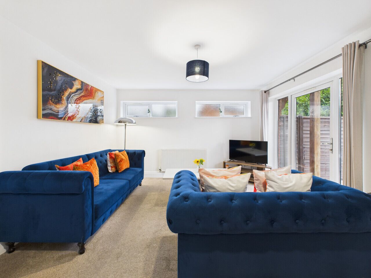 A living room with two blue sofas, a flat-screen TV, and a large abstract painting on the wall.