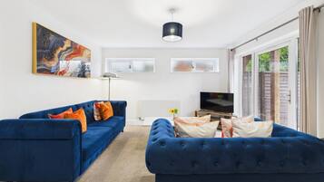 A living room with two blue sofas, a flat-screen TV, and a large abstract painting on the wall.