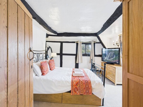 Un dormitorio con cama, almohadas, televisor y un armario de madera.