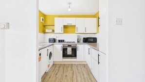 A compact kitchen with white cabinets, a washing machine, a microwave, and a stove. - NEW | Cornfields Place | Racecourse | Free Parking (Bishops Cleeve)