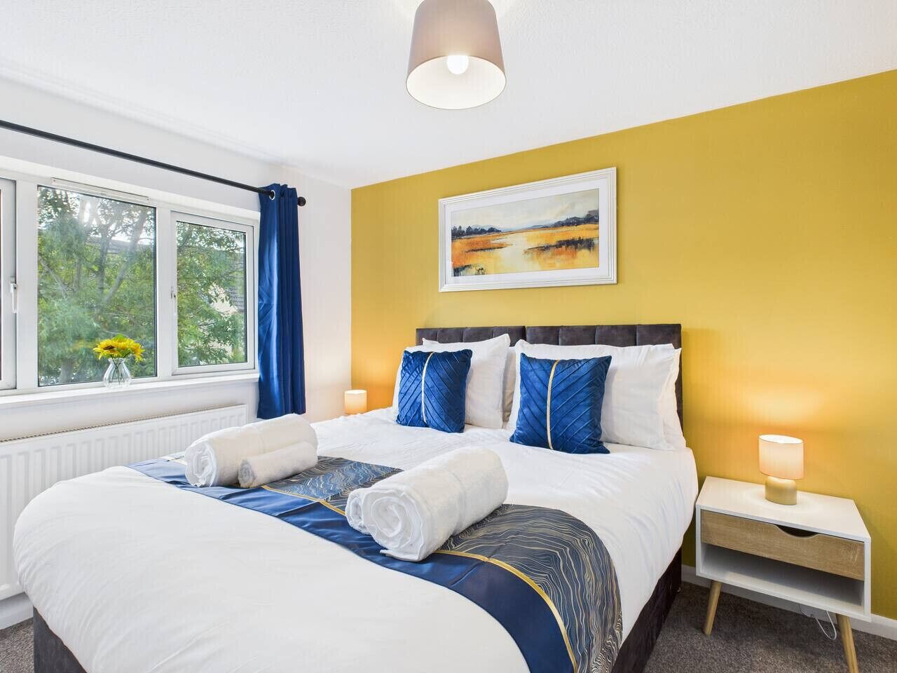 Una habitación de hotel con una cama grande, una mesita de noche, una lámpara y una ventana con cortinas.