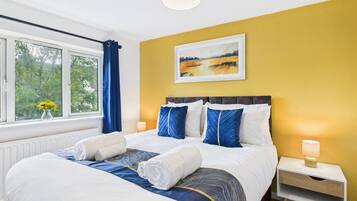 Una habitación de hotel con una cama grande, una mesita de noche, una lámpara y una ventana con cortinas.