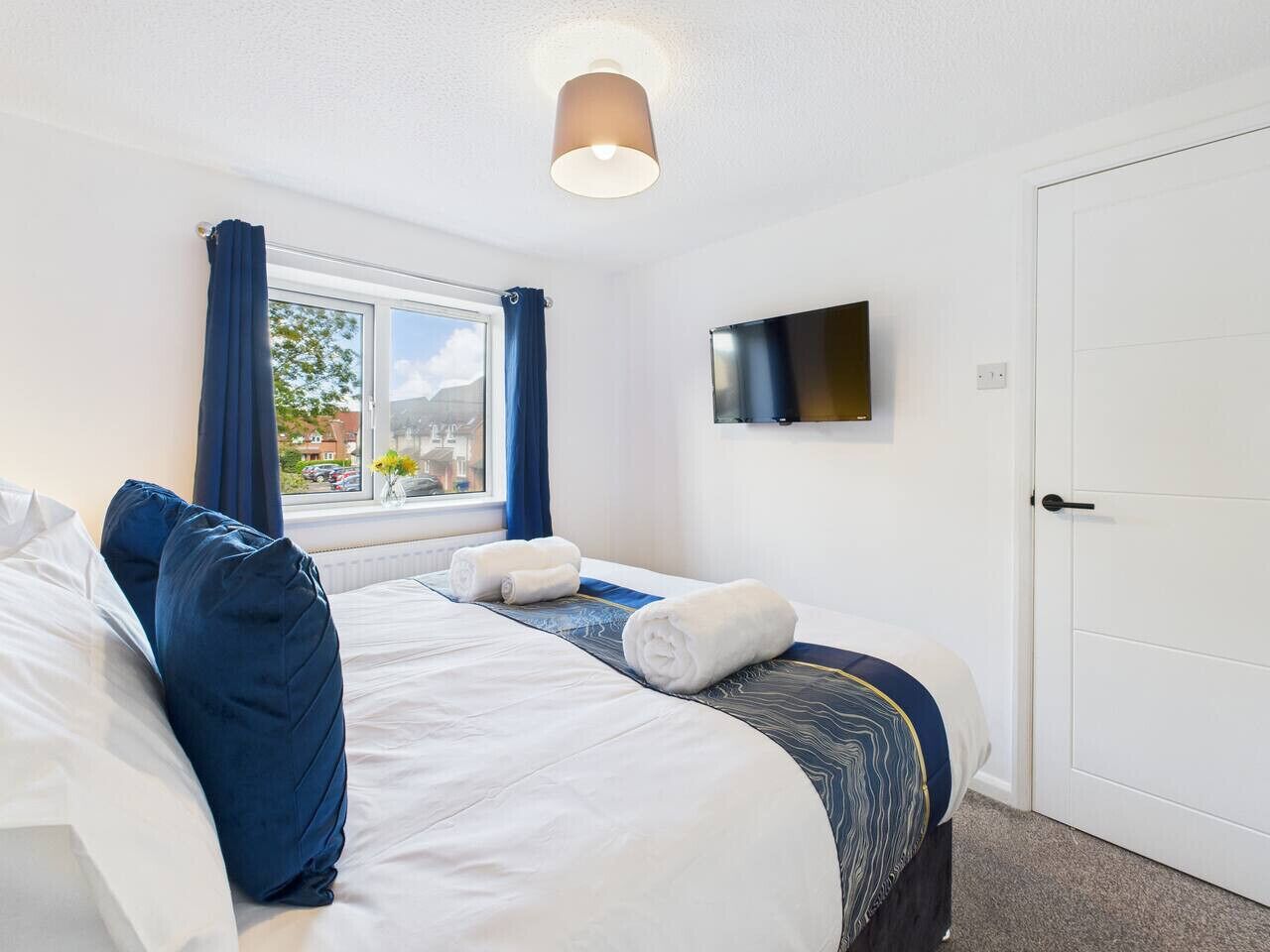 Une chambre d’hôtel avec un grand lit, un téléviseur à écran plat fixé au mur et une fenêtre avec des rideaux.