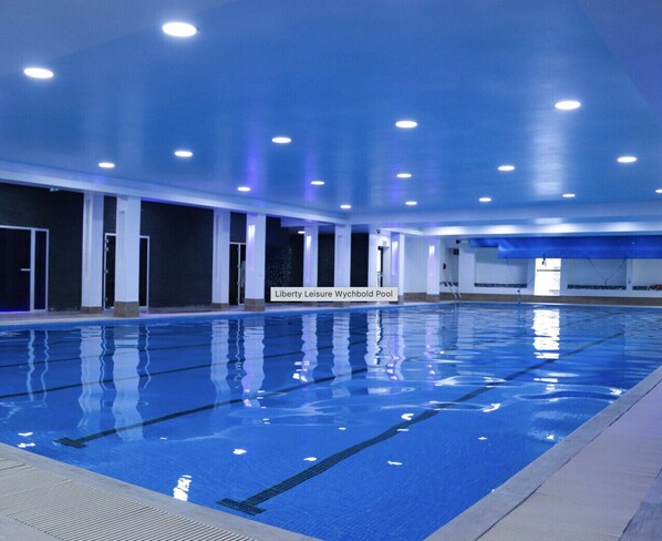 An indoor swimming pool with clear water, surrounded by white pillars and blue lighting. - *New* | No7 Saxon Way | Gym | Pool & Spa (Wychbold)