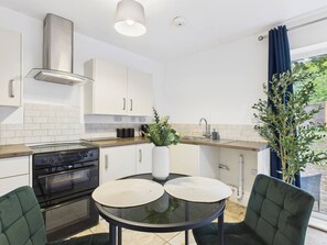 Een moderne keuken met witte kasten, een zwarte kookplaat en een ronde glazen tafel met twee placemats.