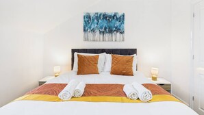 Ein ordentlich bezogenes Bett mit weißer und brauner Bettwäsche, zwei Kissen und einer Decke. Darüber an der Wand hängt ein Bild.