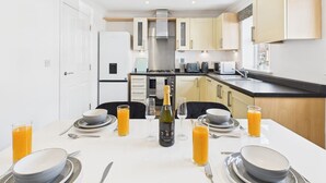 Eine moderne Küche mit weißen Schränken, einer zentralen Kochinsel und einem Essbereich, der für ein Frühstück mit Orangensaft und einer Champagnerflasche gedeckt ist.