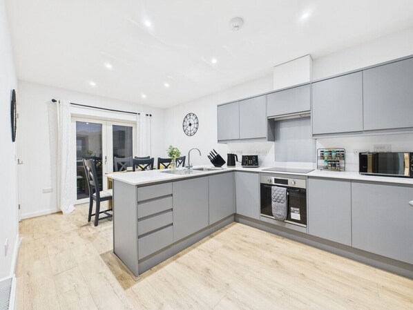 A modern kitchen with grey cabinets, a central island, a built-in oven, and a microwave.