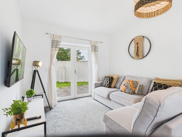 A modern living room with a grey sofa, a flat-screen TV, a tripod lamp, and a large window with curtains.