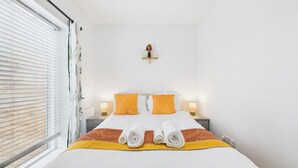 A neatly made bed with white linens, two pillows, and two rolled towels. - Harvey’s Yard | Modern Coastal Home | Sleeps 6 (Cornwall)