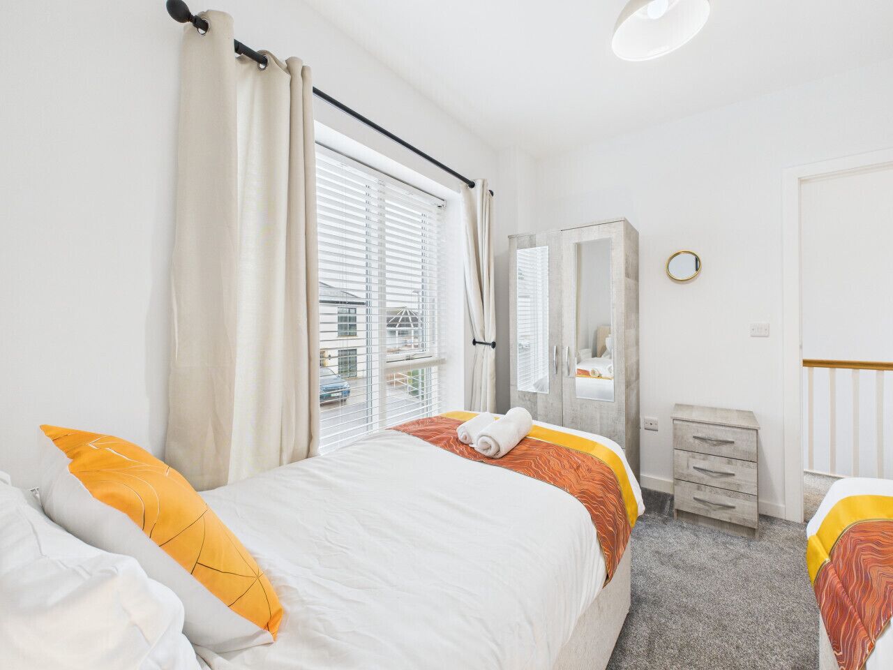 Ein Hotelzimmer mit zwei Betten, einem Schminktisch, einem Spiegel und einem Fenster mit Vorhängen.
