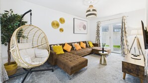A modern living room with a wicker chair, brown sofa, and a small side table. - Harvey’s Yard | Modern Coastal Home | Sleeps 6 (Cornwall)