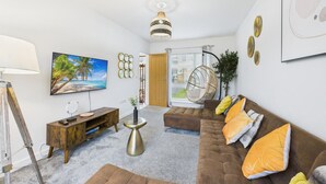 A modern living room with a brown sofa, a hanging chair, a round coffee table, and a TV on the wall. - Harvey’s Yard | Modern Coastal Home | Sleeps 6 (Cornwall)
