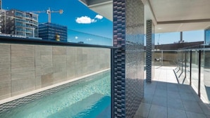 Una piscina con borde de baldosas, barandilla de cristal y vista a una obra en construcción al fondo.