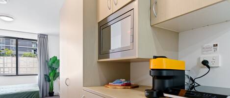 Una kitchenette compacta con microondas, cafetera y toma de corriente.