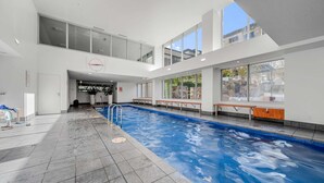 An indoor swimming pool with clear blue water, tiled floor, and benches along the sides. - Glorious Central Canberra 1-bed With Pool & Sauna (Canberra)
