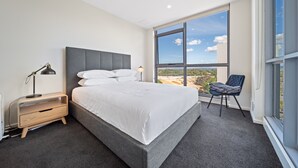 A modern bedroom with a large bed, a nightstand, a chair, and a view of the outdoors through a large window. - Glorious Central Canberra 1-bed With Pool & Sauna (Canberra)