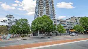 A modern high-rise building with multiple balconies, a pedestrian walkway, and a bus stop. - Glorious Central Canberra 1-bed With Pool & Sauna (Canberra)
