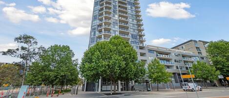 A modern high-rise building with multiple balconies, a pedestrian walkway, and a clear sky.