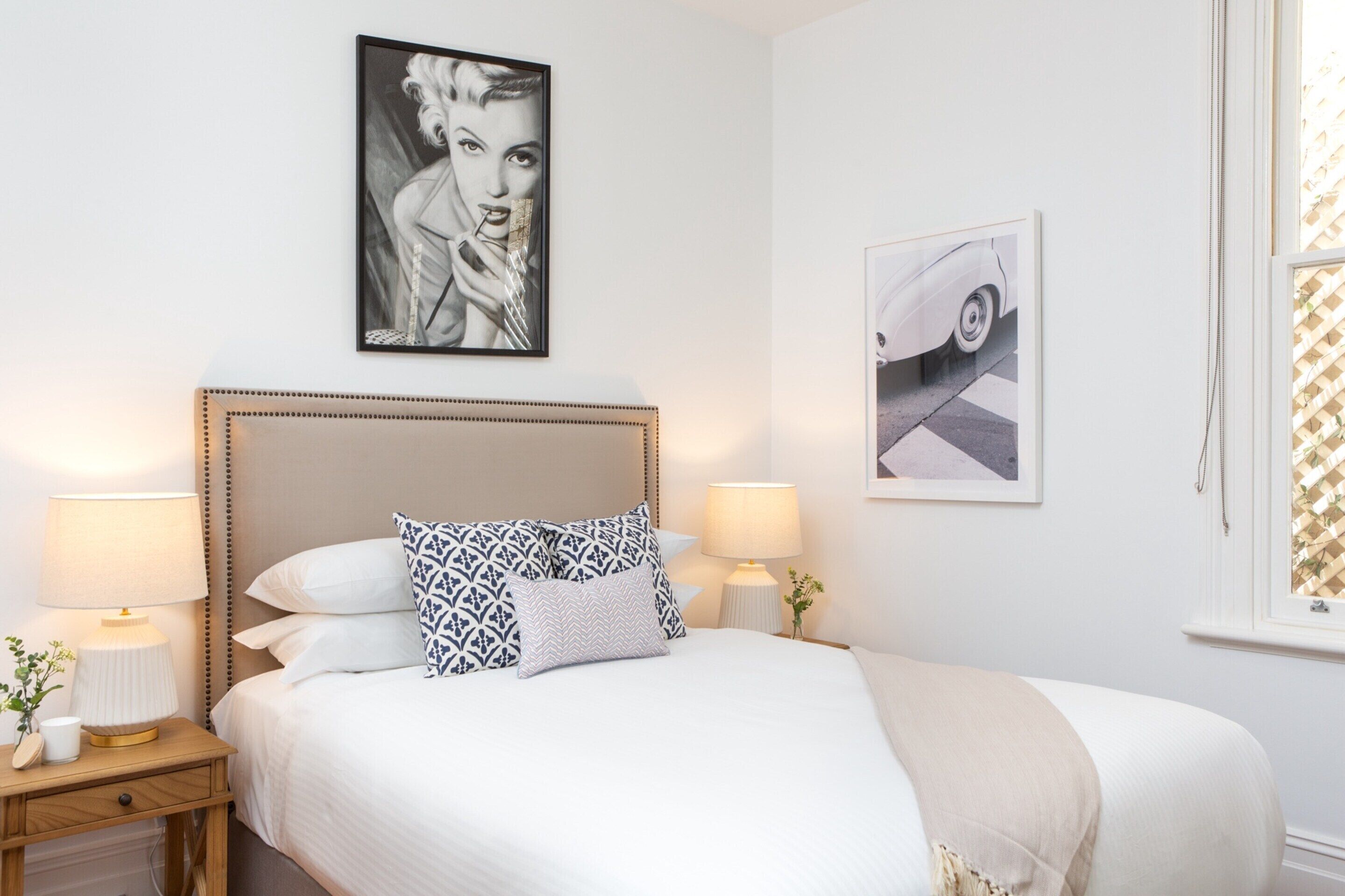 Ein ordentlich eingerichtetes Schlafzimmer mit einem großen Bett, zwei Nachttischen mit Lampen und zwei gerahmten Bildern an der Wand.