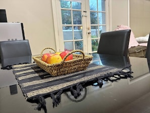 A table with a woven basket containing apples, a black and gold woven placemat, and a glass table. - Cozy Tusmore Apartment With Private Garden City View Near Burnside Village Mall (Adelaide)
