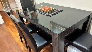 Une table de salle à manger avec un plateau en verre, des chaises noires, un panier de pommes et un appareil électroménager blanc sur la droite.