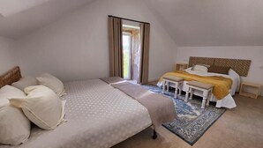 Een slaapkamer met een groot bed, een kleiner bed, een nachtkastje en een raam met gordijnen.