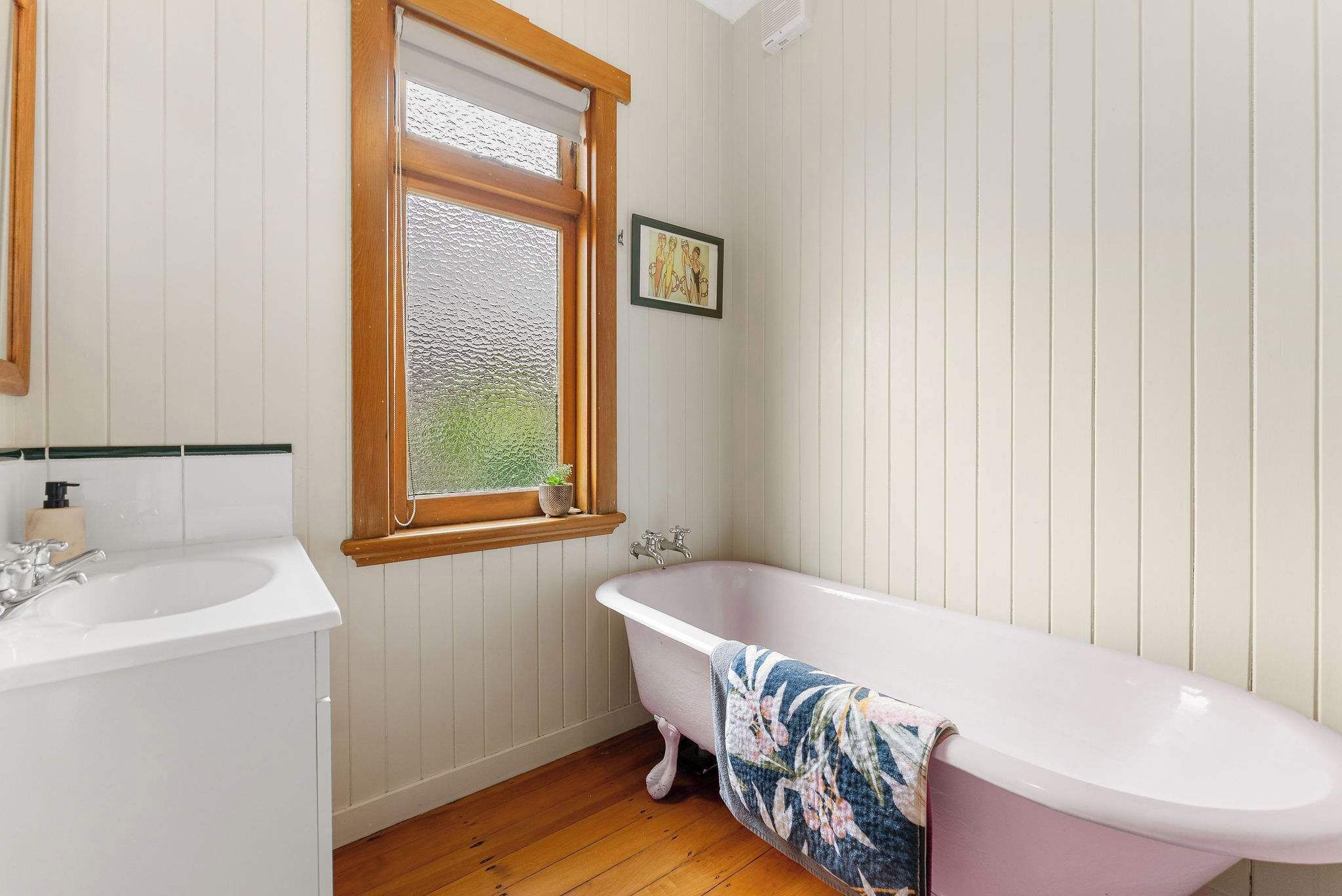 A bathroom with a white bathtub, a wooden window, and a white sink.
