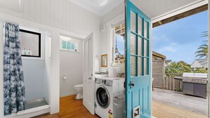 A laundry room with a washing machine and dryer, a toilet, and a blue door leading to an outdoor area with a barbecue grill. - Cabbage Tree Cottage (Tauranga)