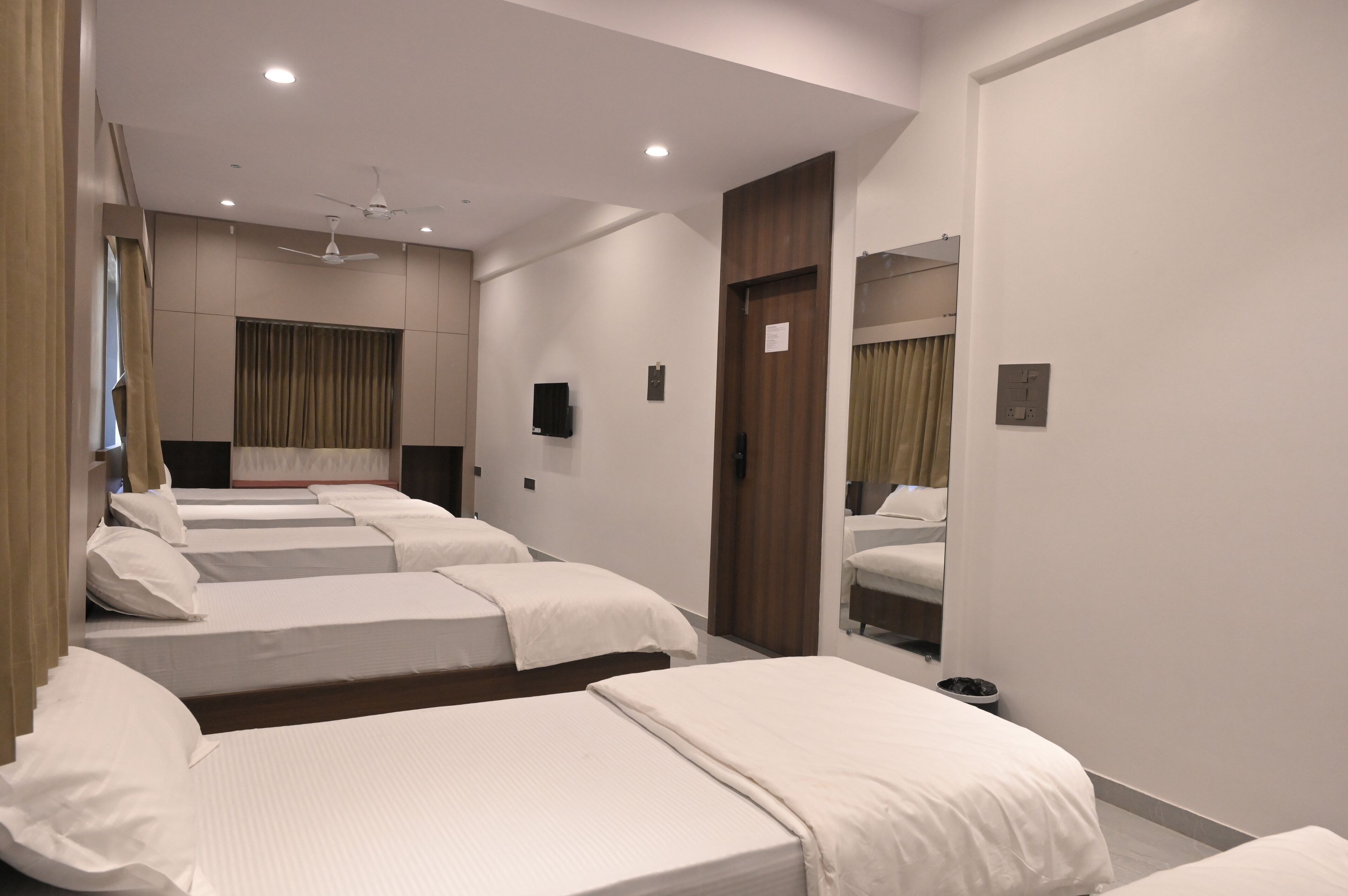 A hotel room with three beds, a ceiling fan, a large mirror, and a door with a sign.