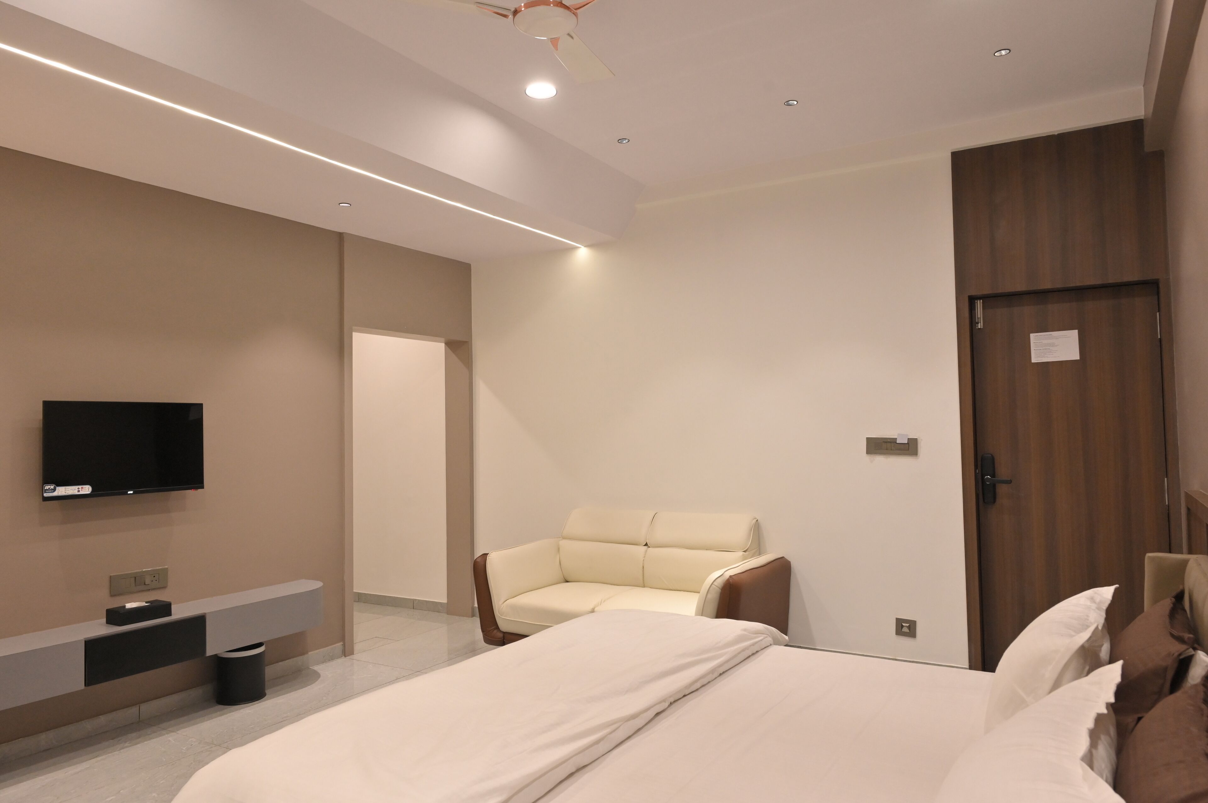 Una habitación de hotel moderna con una cama, un sofá, un televisor montado en la pared y una puerta de madera.