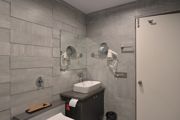Un baño moderno con pared de azulejos grises, un lavamanos blanco y dos espejos fijados a la pared.