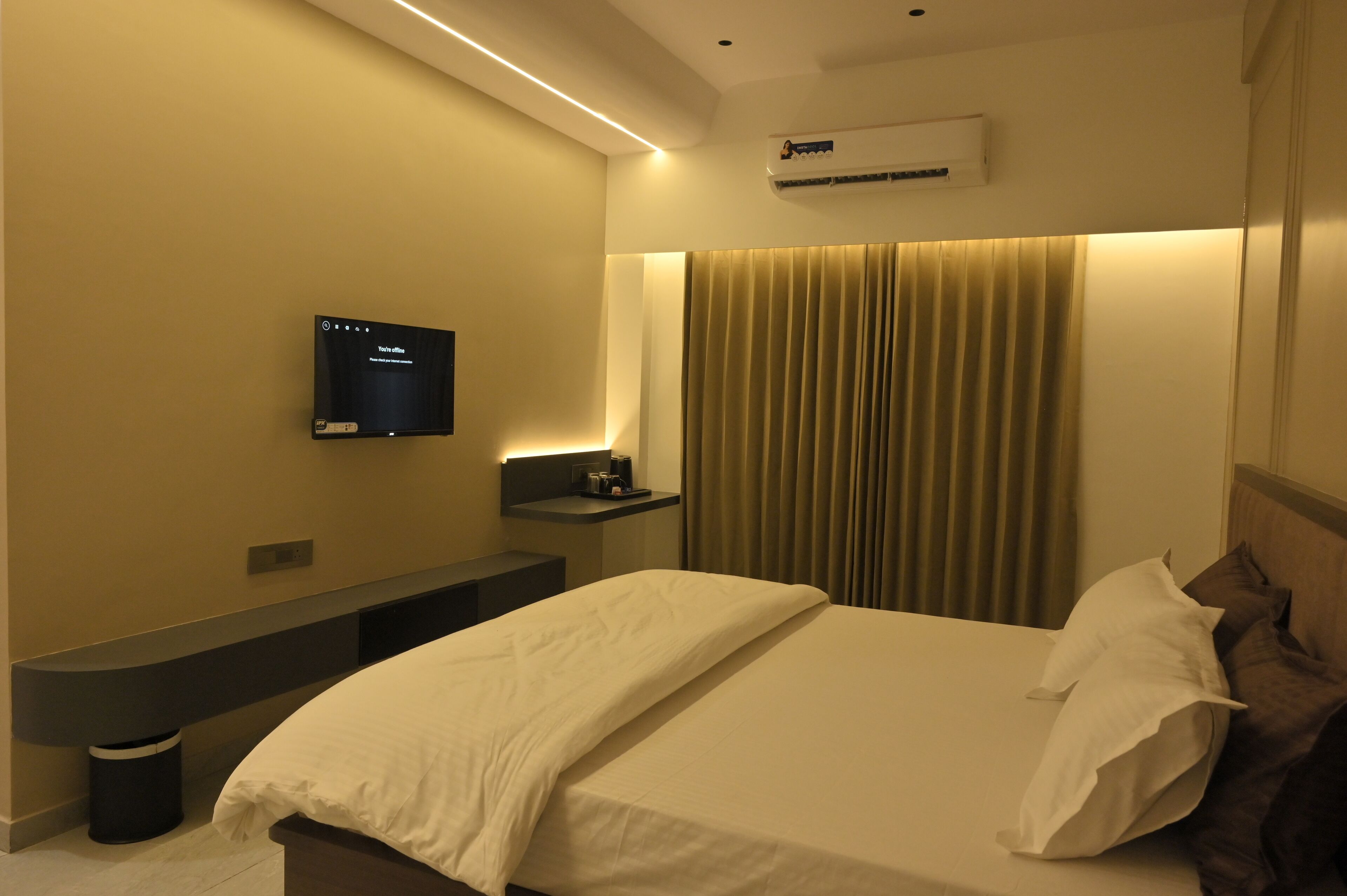A hotel room with a bed, a TV mounted on the wall, a bedside table, and a curtain.