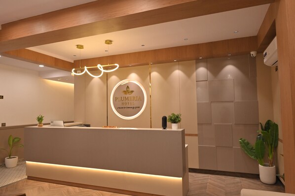 Zona de recepción de un hotel con diseño moderno, que presenta un mostrador de recepción, un logotipo circular y un techo de madera.
